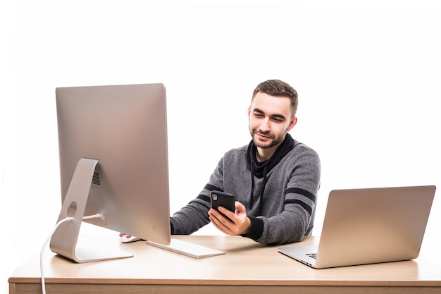 Knappe ondernemer achter zijn bureau met laptop en pc zitten en typen op mobiele telefoon geïsoleerd op wit