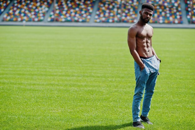 Knappe sexy Afro-Amerikaanse gespierde blote torso man op jeans overall gesteld op groen gras van stadion voetbalveld modieuze zwarte man portret