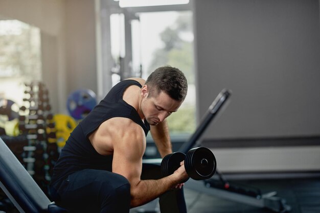 Knappe sportieve man buigen spieren met barbell in donkere sportschool