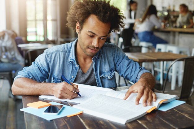 Knappe stijlvolle Afro-Amerikaanse universiteitsstudent studeert in café