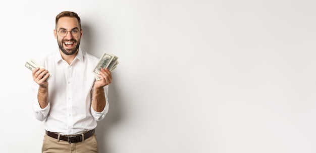 Gratis foto knappe succesvolle zakenman die geld aan het tellen is, zich verheugt en glimlacht terwijl hij op een witte achtergrond staat