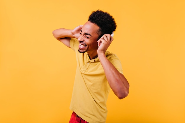 Knappe tevreden man genieten van muziek Indoor foto van trendy zwart mannelijk model in oortelefoons dansen op gele achtergrond