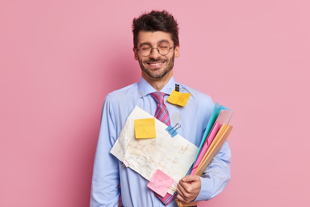 Knappe tevreden vrolijke onervaren zakenman glimlach houdt gelukkig mappen met documenten bedekt met stickers draagt formele overhemd en stropdas bereidt zich voor op onderhandelingen of ontmoeting met collega's