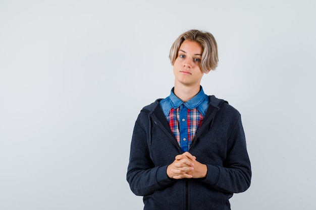 Knappe tienerjongen die gevouwen handen voor hem houdt in hemd, hoodie en er intelligent uitziet. vooraanzicht.