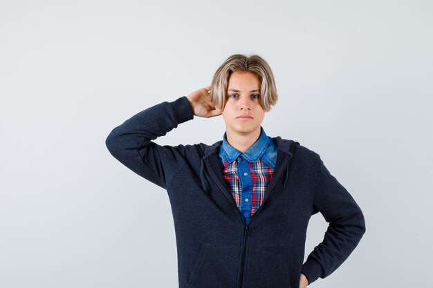 Knappe tienerjongen met hand achter hoofd in overhemd, hoodie en peinzend kijkend. vooraanzicht.