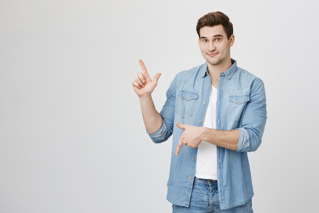 Knappe vrolijke mannelijke student die op en neer op banners wijst