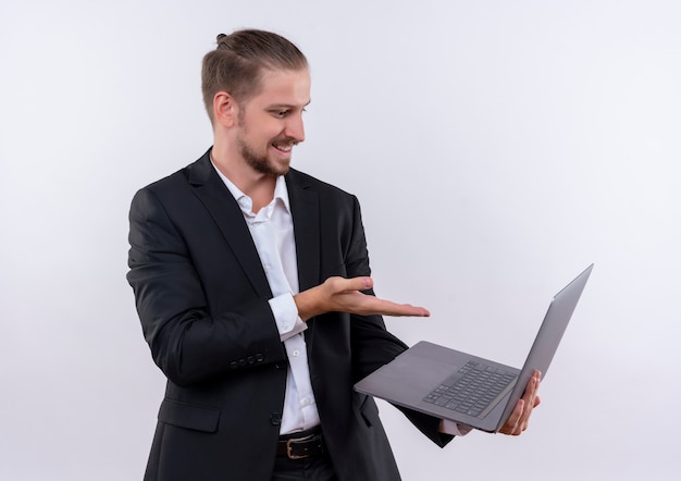 Knappe zakenman dragen pak met laptop computer wijzend met arm naar scherm wioth glimlach op gezicht staande op witte achtergrond