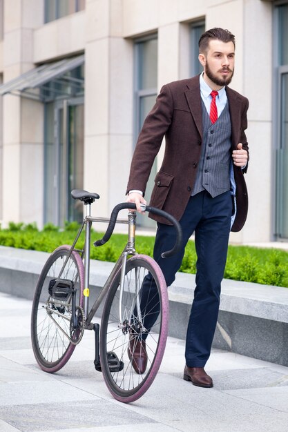 Knappe zakenman in een jas en een rode stropdas en zijn fiets op stadsstraten.