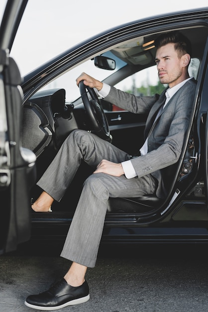 Knappe zakenmanzitting in de auto met open deur