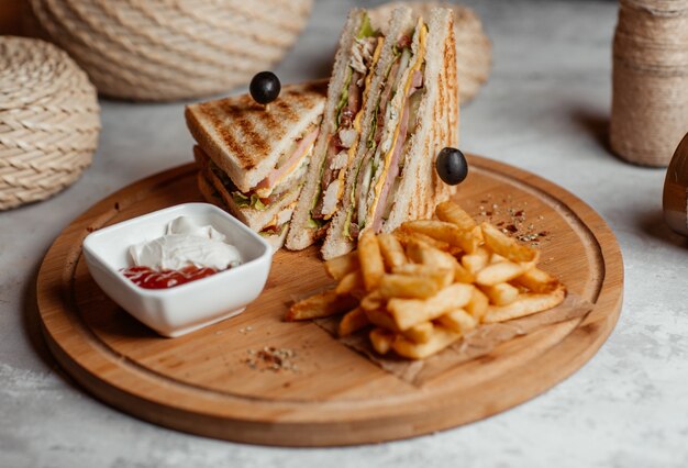 Knapperige frietjes, snacks, stokjes en clubsandwiches met ketcup op een houten bord