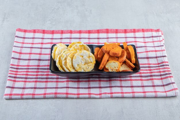 Knapperige volkoren rijstwafels en crackers op zwarte plaat.