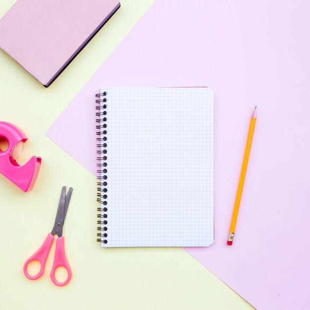 knolling bureau samenstelling met een notebook, potlood, schaar en boek over roze en geel terug naar school