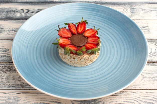 koekje met aardbeien en ronde chocolade in blauw bord op rustiek grijs