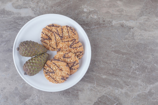 Koekjes en dennenappels op een schotel op marmer