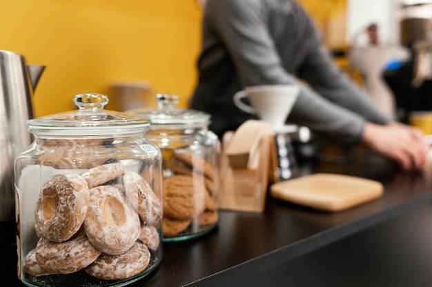 Koekjes en lekkernijen op de toonbank van de coffeeshop met onscherpe mannelijke barista