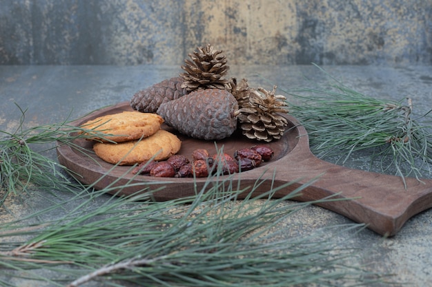 Koekjes, gedroogde rozenbottels en dennenappels op een houten bord. hoge kwaliteit foto