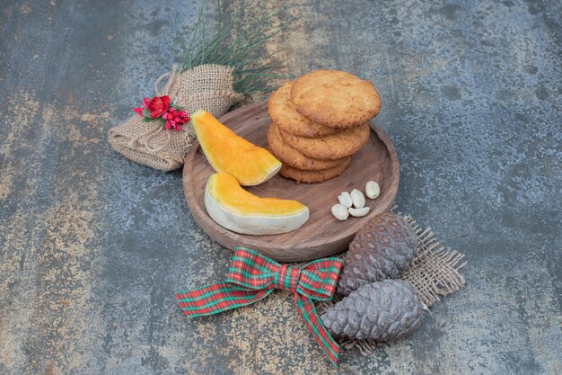 Koekjes met dennenappels en twee plakjes pompoen op houten plaat.