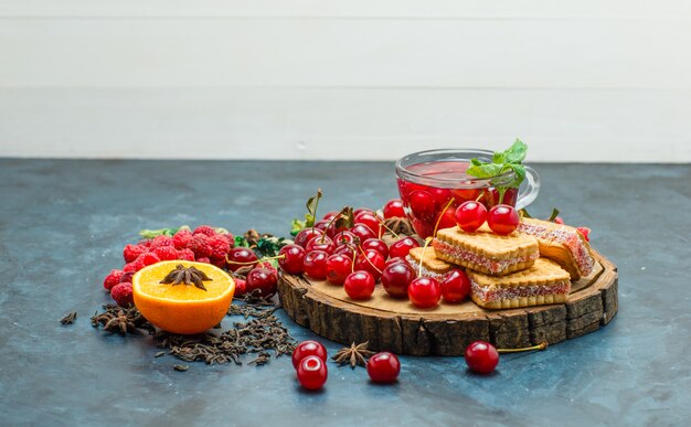 Koekjes met kruiden, fruit, thee, specerijen, bord op wit en stucwerk achtergrond, zijaanzicht.