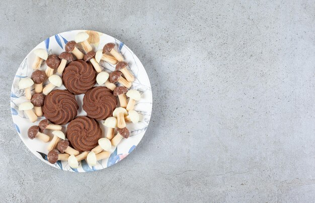 Koekjes omgeven door chocoladepaddestoelen op een bord op marmeren achtergrond.