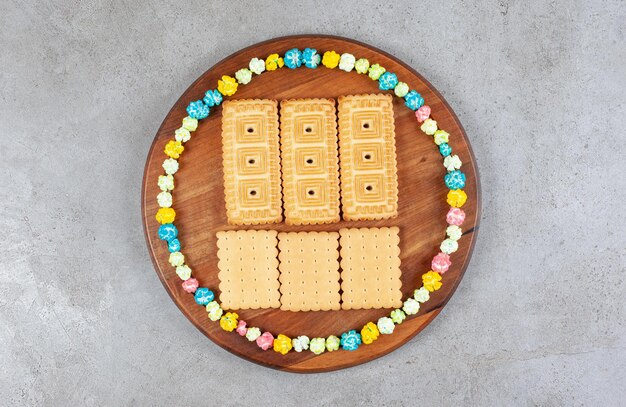 Koekjes omringd door snoepjes in een cirkel op een houten bord op marmeren achtergrond. Hoge kwaliteit foto