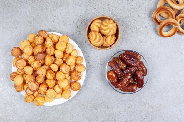 Koekjes op een bord en in een kom naast wat gebonden sushki en een handvol dadels op een marmeren ondergrond