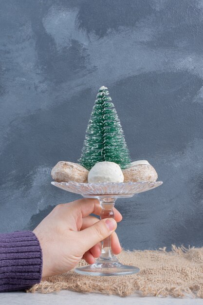 Koekjes rond een boombeeldje op een klein voetstuk, vastgehouden door een hand op een marmeren oppervlak