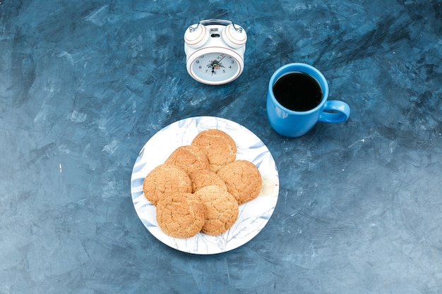 Koekjes, wekker en koffiekopje op een donkerblauwe achtergrond