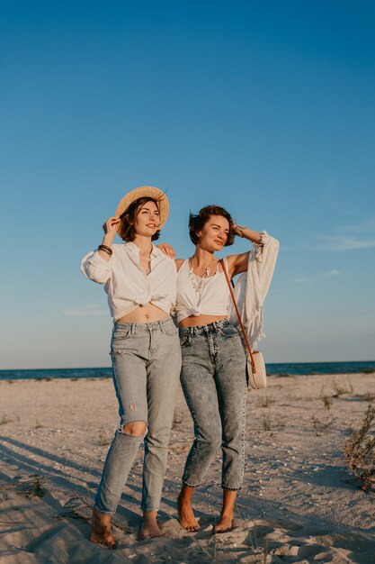 Koele twee jonge vrouwen die plezier hebben op het zonsondergangstrand, homo-lesbische liefdesromantiek