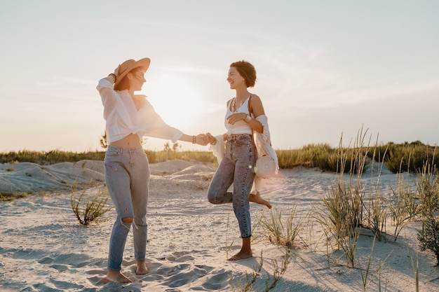 Koele twee jonge vrouwen die plezier hebben op het zonsondergangstrand, homo-lesbische liefdesromantiek