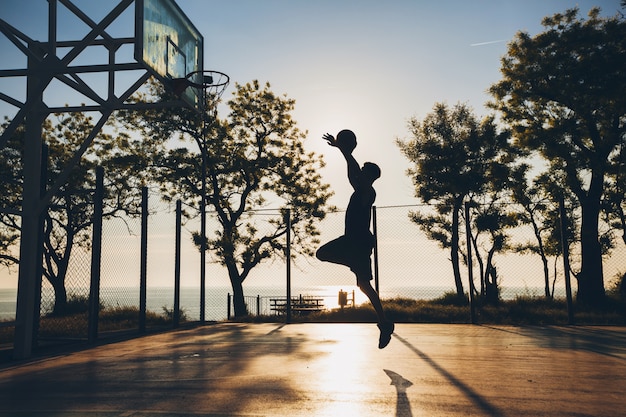 Koele zwarte man die sport doet, basketbal speelt bij zonsopgang, silhouet springt