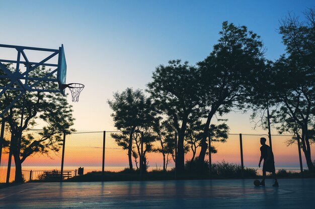 Koele zwarte man die sport doet, basketbal speelt op zonsopgang, silhouet