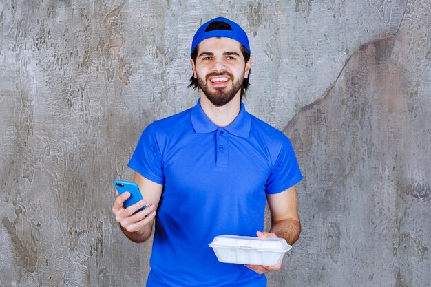 Koerier in blauw uniform met een plastic afhaaldoos en nieuwe bestellingen via de telefoon.