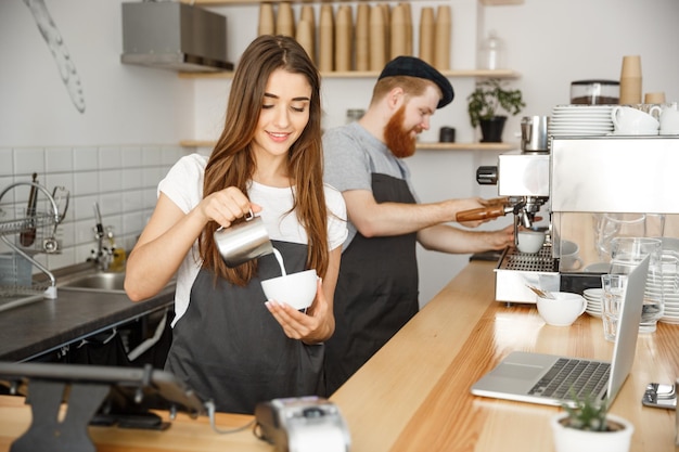 Koffie business concept close-up dame barista in schort melk voorbereiden en gieten in hete kop terwijl ze in café staat