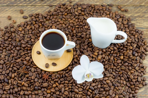 Koffie een klein kopje aromatische koffie tegen de achtergrond van koffiebonen, melkkannetje, orchideebloem. het concept van een dorpsontbijt in de ochtend.