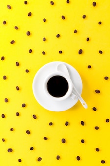 Koffie espresso in kleine witte keramische beker met veel koffiebonen op gele levendige achtergrond.