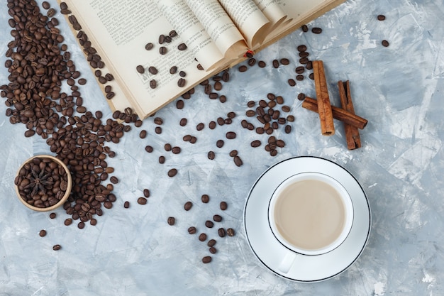 Koffie in een kopje met koffiebonen, boek, kaneelstokjes bovenaanzicht op een grijze gips achtergrond