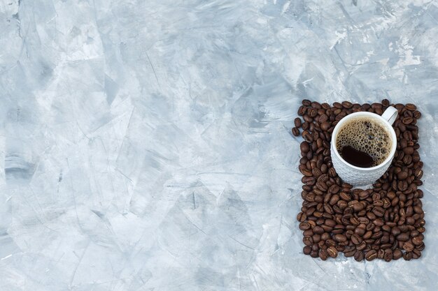 Koffie in een kopje met koffiebonen plat lag op een blauwe marmeren achtergrond