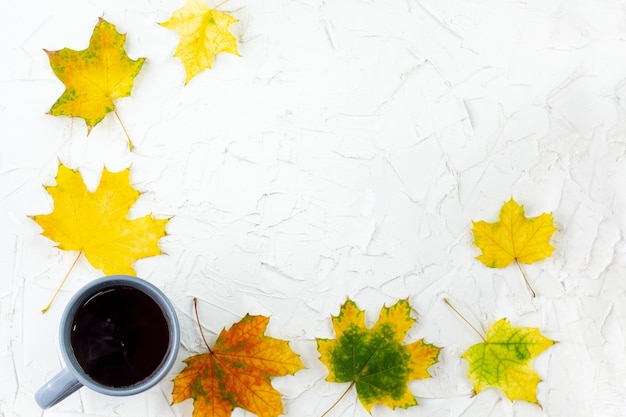 Koffie in grijze kop met herfstgele esdoornbladeren op witte tafel