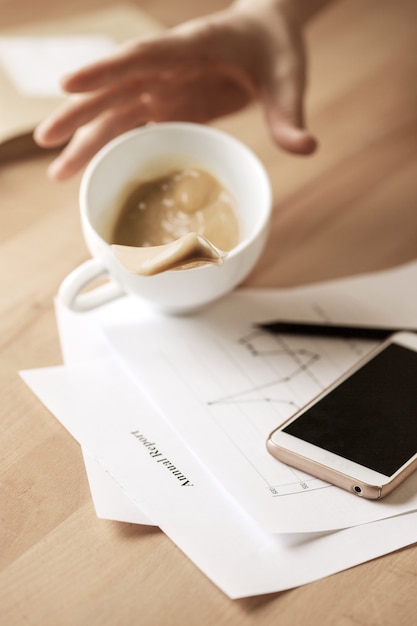 Koffie in witte kop die op de lijst in de ochtend bij bureaulijst morsen