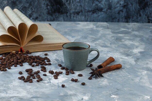 Koffiebonen in een houten kom met boek, kaneel, kopje koffie close-up op een lichte en donkerblauwe marmeren achtergrond
