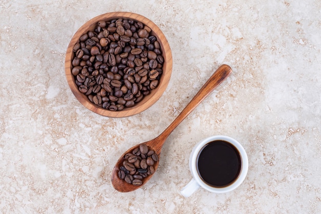 Koffiebonen in een kom en op een lepel naast een kopje koffie