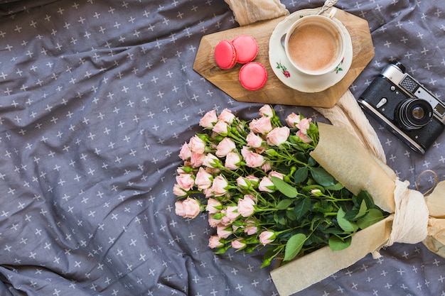 Koffiekop; bitterkoekjes; camera en bloemboeket op tafelkleed