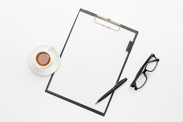 Gratis foto koffiekop en pen met witboek op klembord tegen bureau