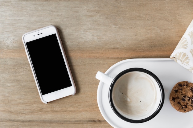 Koffiekop met koekje op wit dienblad en smartphone op houten achtergrond