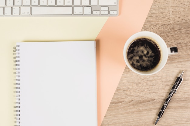 Koffiekop; pen; toetsenbord; en spiraalvormig notitieboekje op gekleurde en houten achtergrond