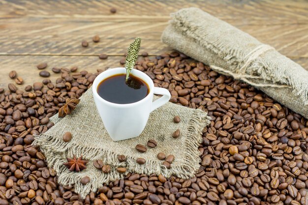 Koffiekopje met aromatische zwarte koffie op een jute servet en koffiebonen. houten rustieke achtergrond. Premium Foto