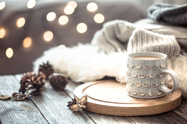 Koffiekopje over Kerstverlichting bokeh in huis op houten tafel met trui op een muur en decoraties. Vakantie decoratie