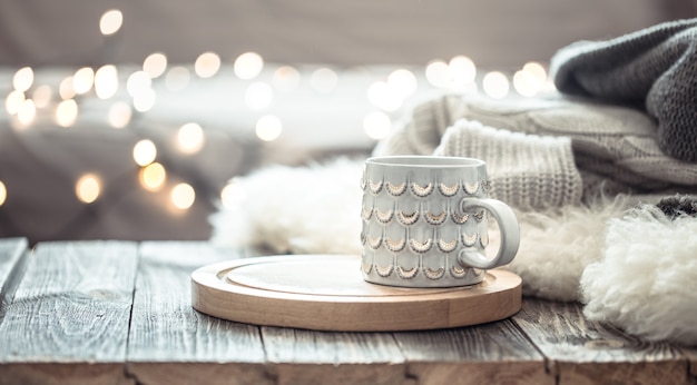 Gratis foto koffiekopje over kerstverlichting bokeh in huis op houten tafel met trui op een muur. vakantiedecoratie, magische kerstmis