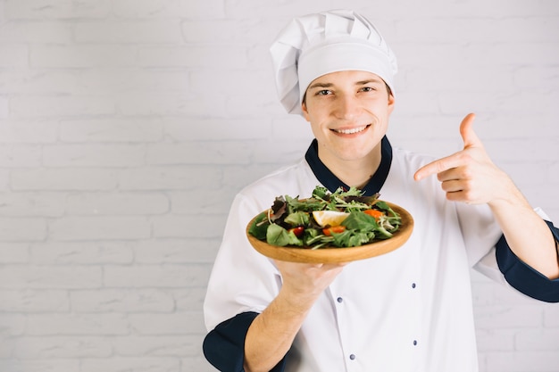 Gratis foto kok wijzende vinger op salade op houten plaat