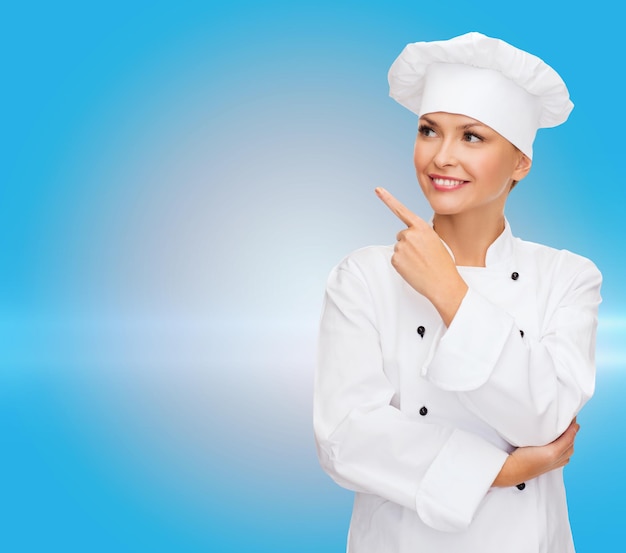 Koken, reclame en voedselconcept - glimlachende vrouwelijke chef-kok, kok of bakker wijzende vinger naar iets